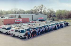 Photo from 1974 of Hanna Inc and its large staff standing in front of 2 long rows of hvac trucks and vans at the Wichita location