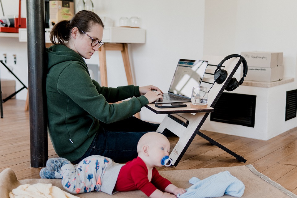 Mom working on floor with laptop with baby, not an ideal home office. Photo by Standsome Worklifestyle on Unsplash